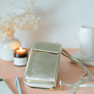 Gold Leather Phone Purse with a lit candle on a peach able