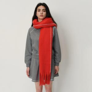 Red scarf with blanket stitching worn by a women with a grey coat and dark hair.