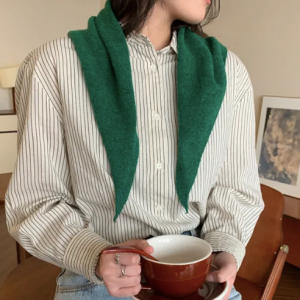 Woman in a cream blouse wearing a green triangle knit scarf draped over her shouders.