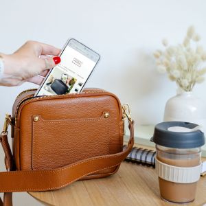Tan leather double zip bag on a table with a coffee