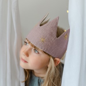 little girl with her lilac linen crown looking between the curtains